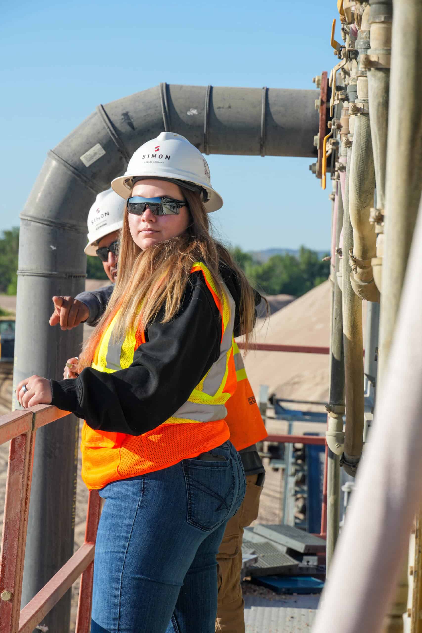 Woman looking over shoulder with vest and hard hat on.