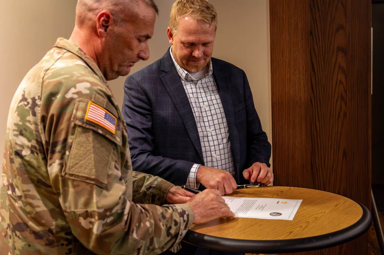 2 men, one in a suit and one in a military uniform signing forms. 