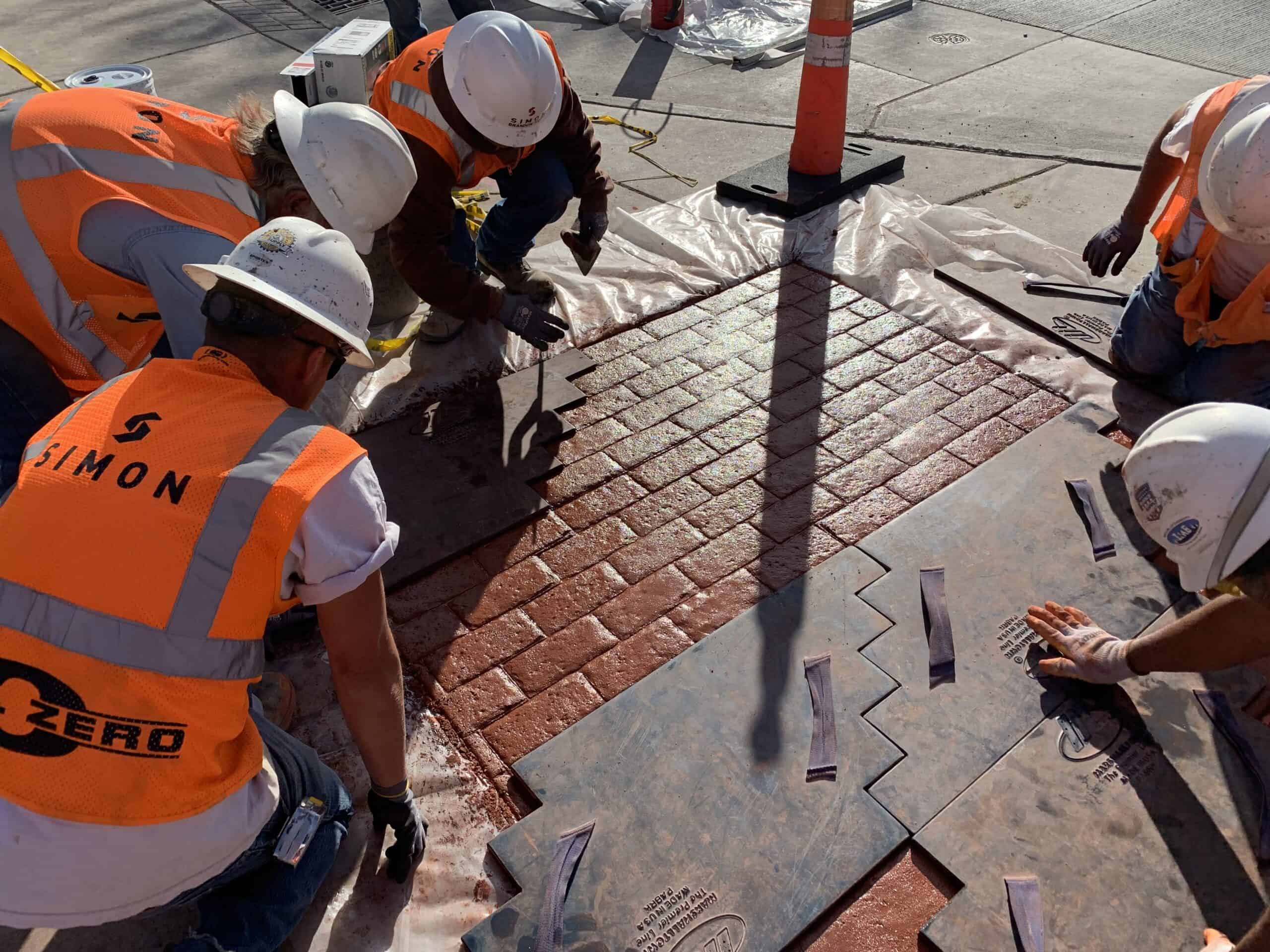 Simon workers in vest and hardhat working on sidewalk.