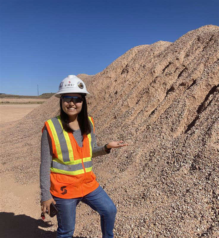 A woman in a safety vest and hard hat standing in front of a pile of gravel