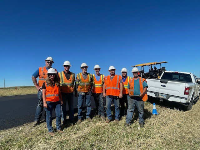Construction team posing together in safety vests and hard hats on a job site.