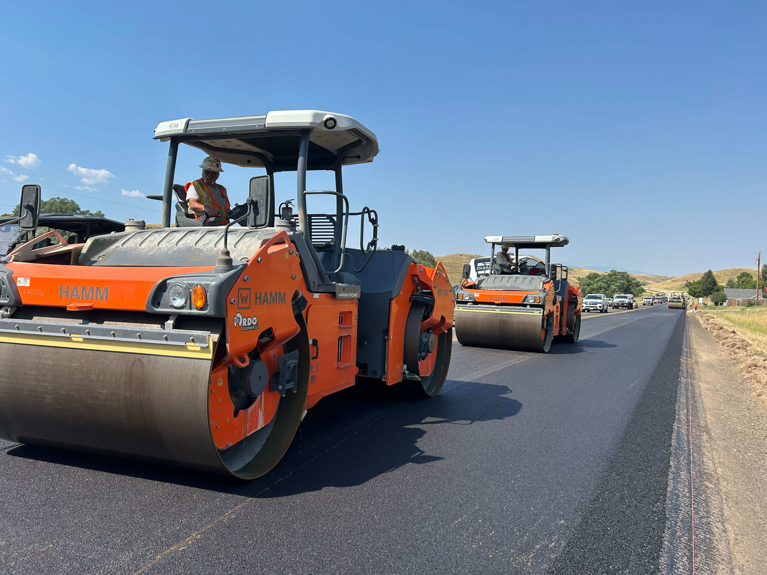 Two rollers paving a newly asphalted road with blue skies in the background.