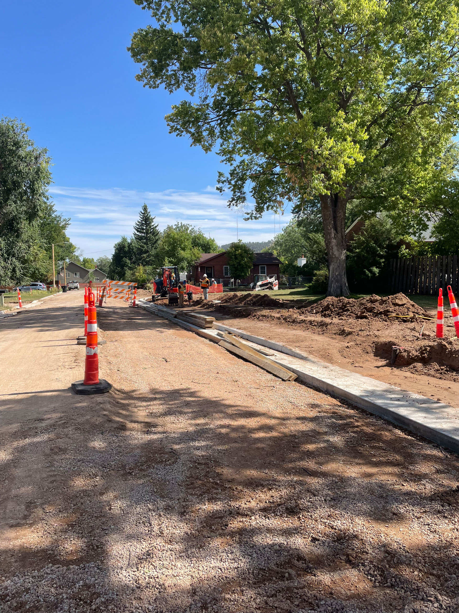 Construction site with roadwork and traffic cones under clear blue skies and trees.