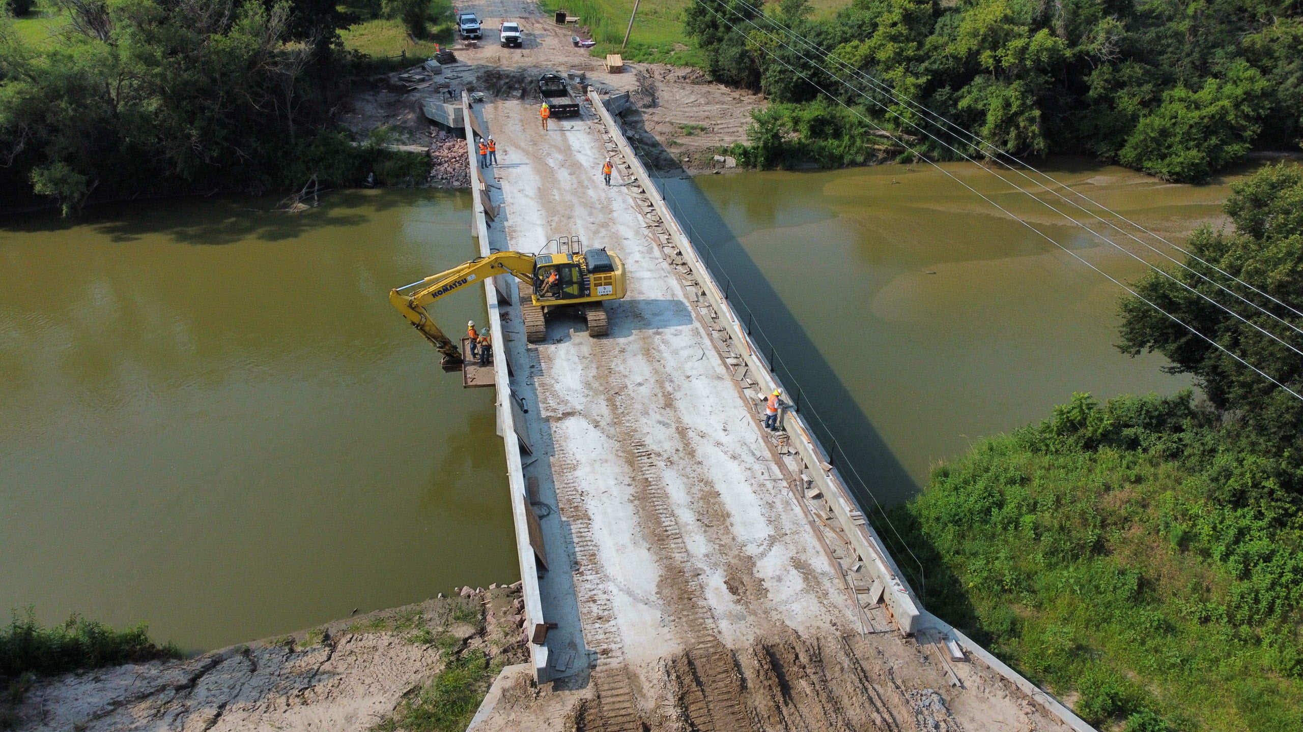Construction workers building a bridge over a river with construction equipment nearby